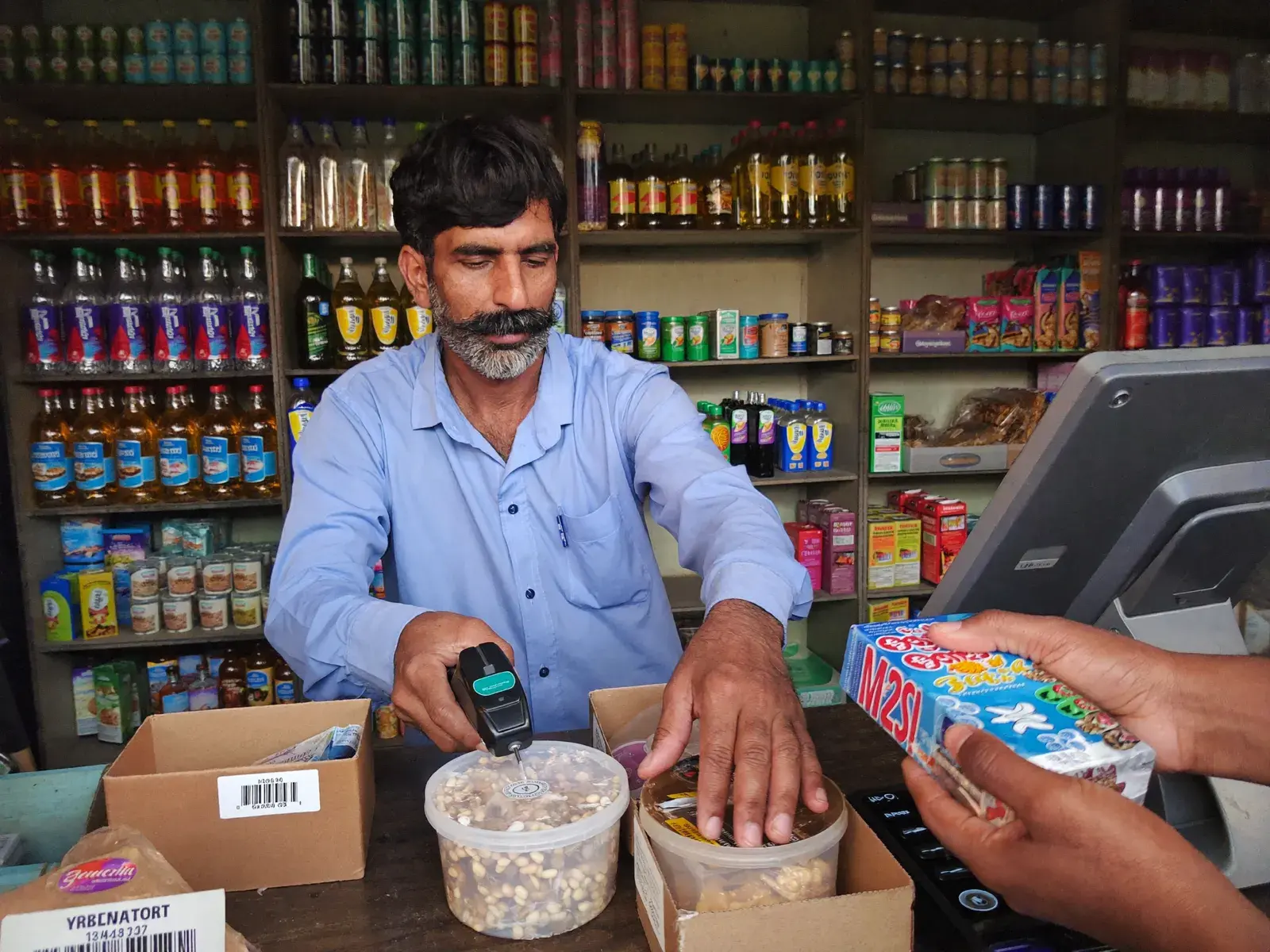 Shopkeeper scanning a product at a counter lined with stocked shelves
